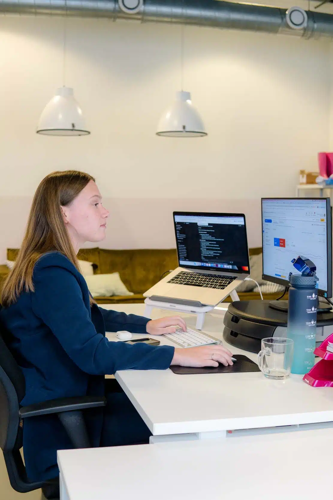 BURO210 Fullservice Marketingbureau Jonge vrouw werkt geconcentreerd aan haar bureau met laptop en monitor. Programmeur of data analist in een moderne kantooromgeving.